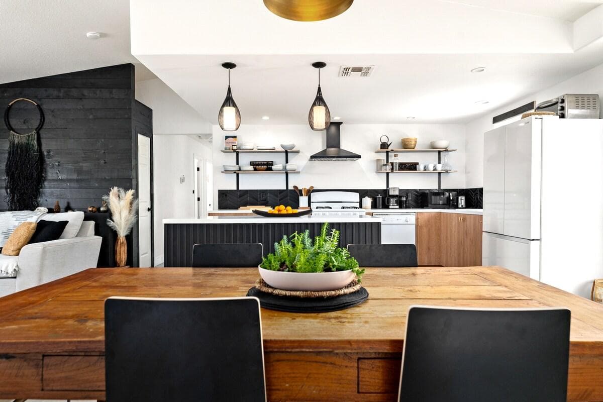 Stylish open kitchen and dining space with a modern color palette. Matte black finishes, aged wood tones, and soft hints of dusty pink.